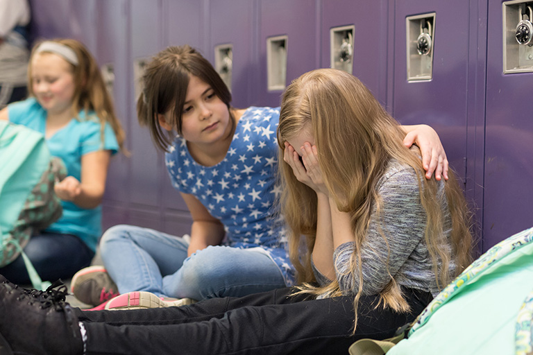 Student consoling an upset friend by school lockers.